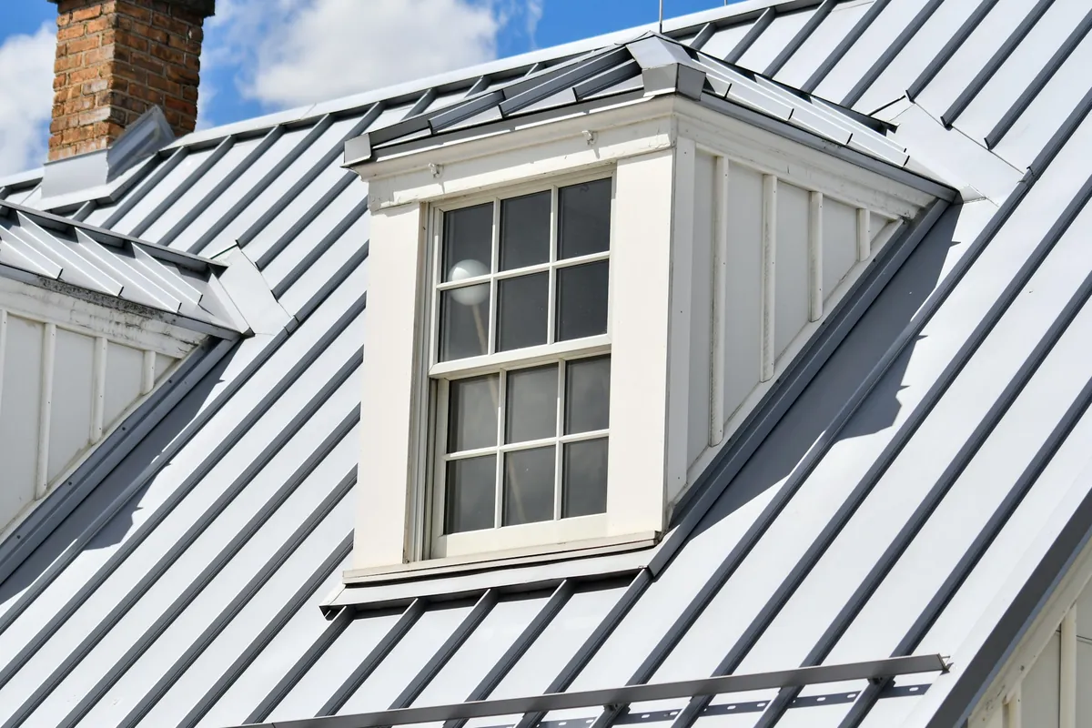 A white dormer window set into a standing seam metal roof