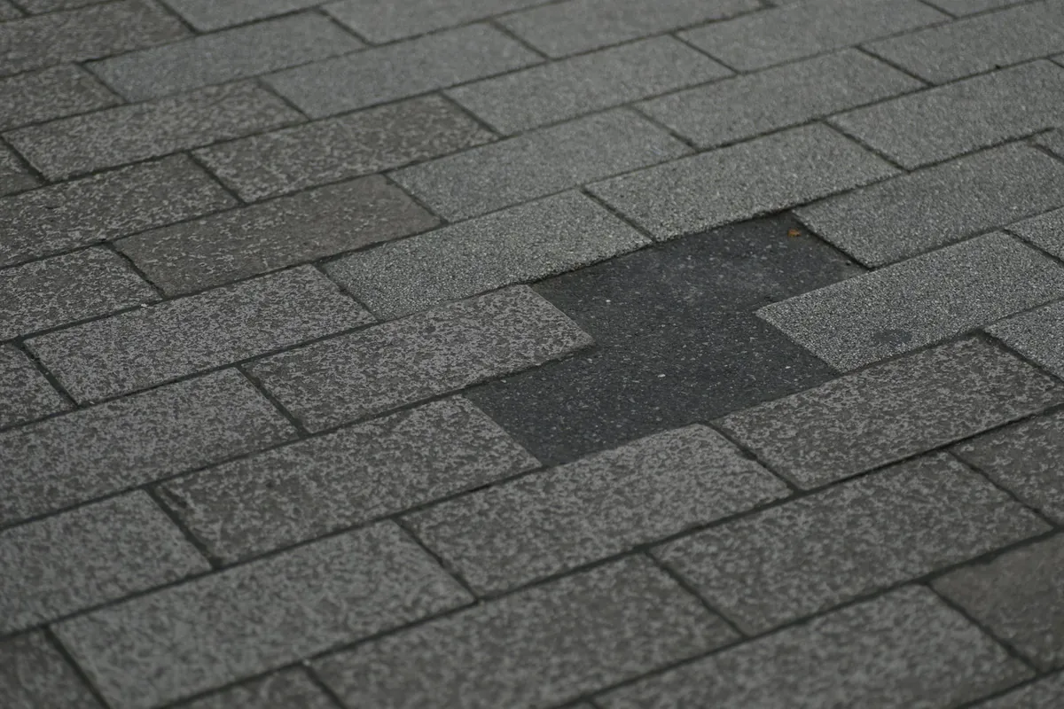 Close-up of gray asphalt shingles with a damaged, bare patch